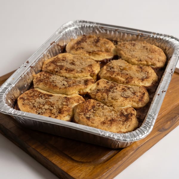 Baked apple fritters with cinnamon sugar topping in a foil pan on a wooden board.